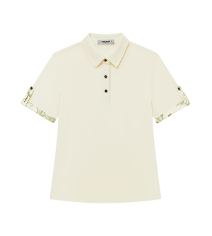 A short-sleeve polo shirt in cream-colored piqué fabric, featuring green botanical patterns printed on the cuffs and collar, with a three-button placket. 